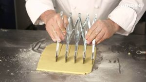Multi-wheel pasta cutter slicing uniform strips for fettuccine on a kitchen counter.