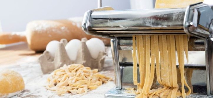 Manual pasta maker with dough being rolled out on a kitchen counter.