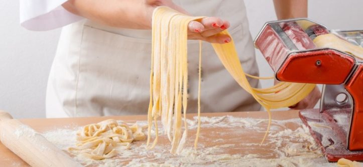 Home cook fixing a jammed pasta maker on a kitchen counter.