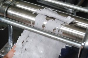 Close-up of a pasta maker roller being cleared of stuck dough.