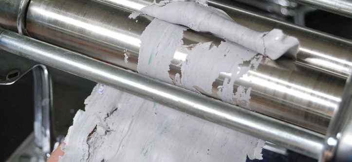 Close-up of a pasta maker roller being cleared of stuck dough.