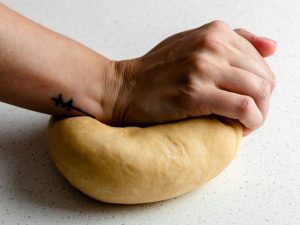 Home cook troubleshooting sticky or torn pasta dough on a work surface.