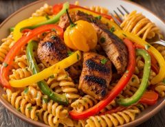 A bowl of creamy rasta pasta with colorful bell peppers and jerk-seasoned chicken on a wooden table