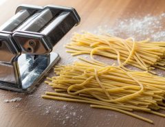 Freshly cut homemade spaghetti strands resting on a floured wooden surface next to a manual pasta maker