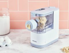 Philips pasta maker on kitchen counter extruding fresh homemade spaghetti dough.