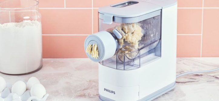 Philips pasta maker on kitchen counter extruding fresh homemade spaghetti dough.