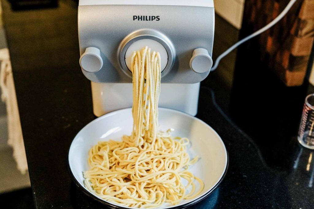 Automatic Philips pasta maker preparing fresh pasta with flour and dough ingredients nearby.