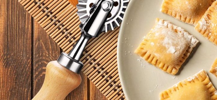 Stainless steel pasta cutter wheel slicing fresh dough into neat strips on wooden board.