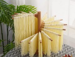 Wooden pasta hanging rack with fresh homemade noodles drying evenly in a bright kitchen.