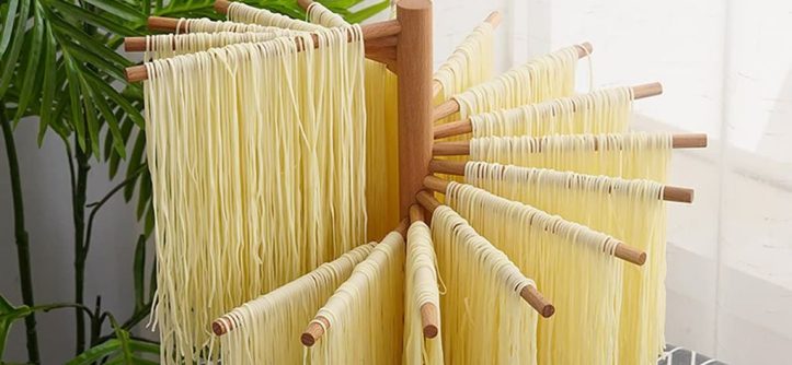 Wooden pasta hanging rack with fresh homemade noodles drying evenly in a bright kitchen.