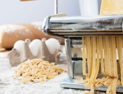 Fresh homemade pasta being prepared using a hand-crank pasta machine setup