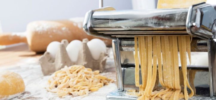 Fresh homemade pasta being prepared using a hand-crank pasta machine setup