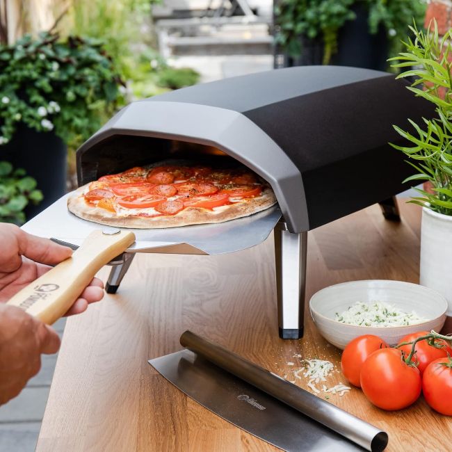 Chef Pomodoro pizza peel transferring a freshly baked pizza from an Ooni oven to a serving board